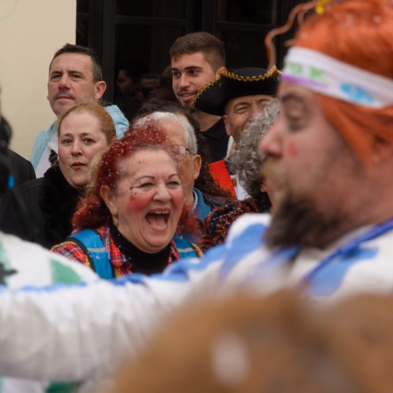 Escena de carnaval, chirigota callejera, mujer y hombre serios al fondo de la imagen mientras el resto se ríe