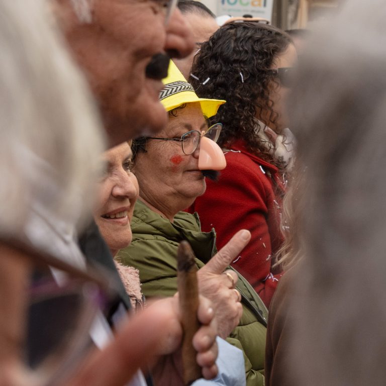 Entre la multitud, se aprecia el perfil de una mujer mayor, disfrazada con un gorro amarillo y una nariz falsa