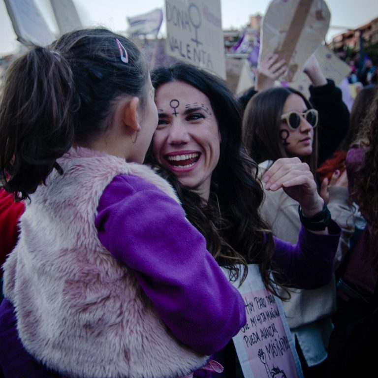 Mujer sujetando una niña pequeña en una manifestación feminista, se miran y se ríen