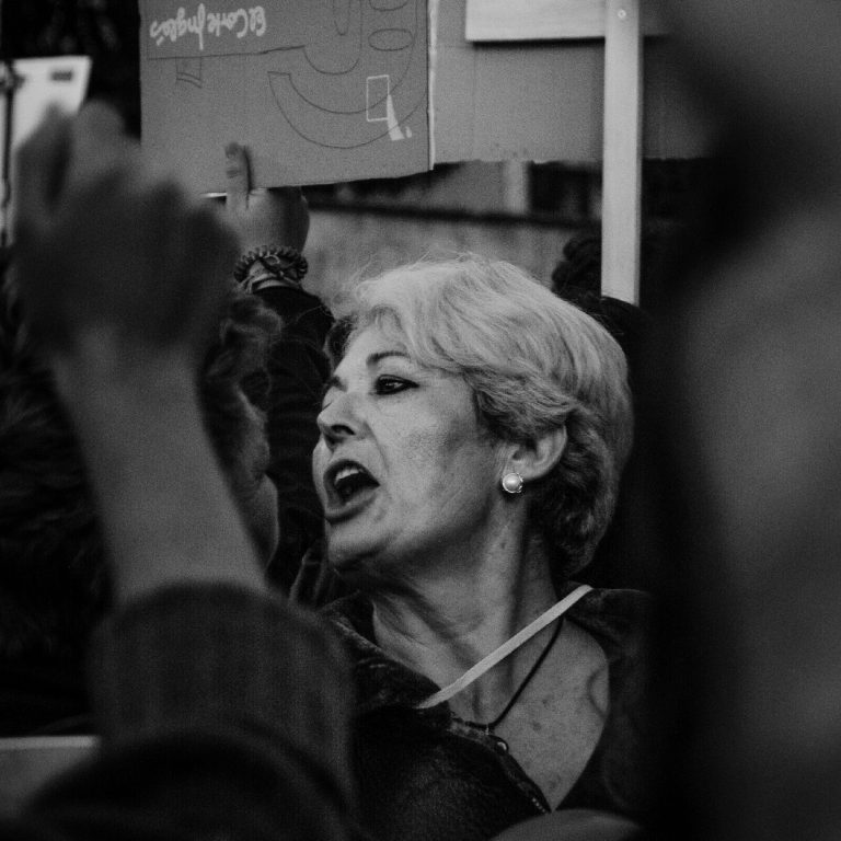 Mujer anciana, gritando en una manifestación feminista, rodeada de brazos en alto y carteles