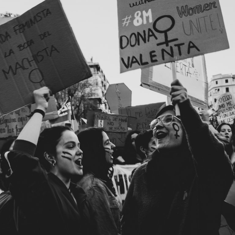 Dos mujeres jóvenes en una manifestación feminista sujetando carteles, gritando y riendo